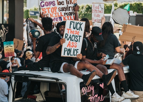 Protesters holding signs, sitting on top of cars